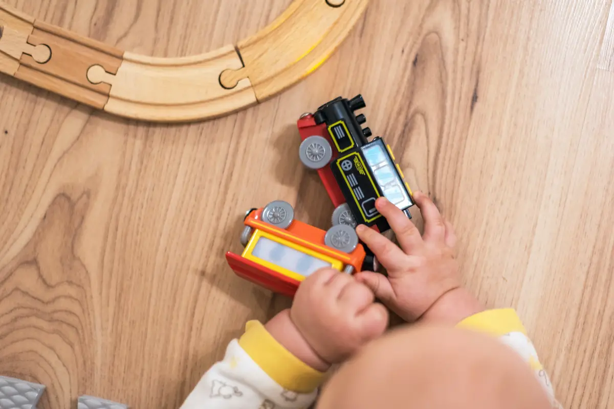 Baby has tummy time on the floor and plays with wooden trains and train track.